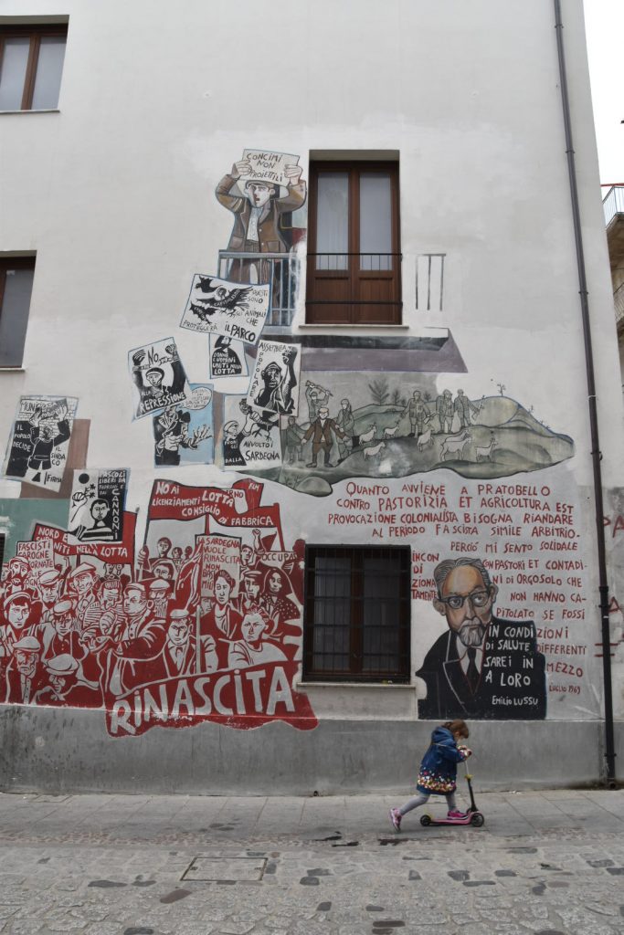 Mural depicting Emilio Lussu's comments about local Orgosolo's occupation by military forces in 1969... the little girl glides past unaware...